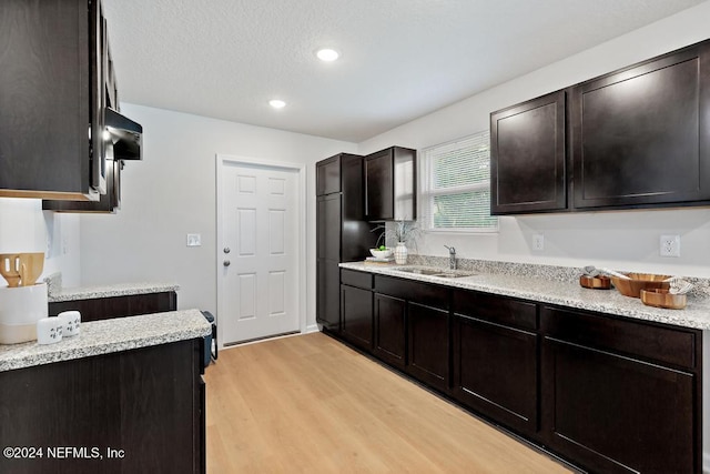 kitchen with light stone countertops, dark brown cabinets, light hardwood / wood-style floors, and sink