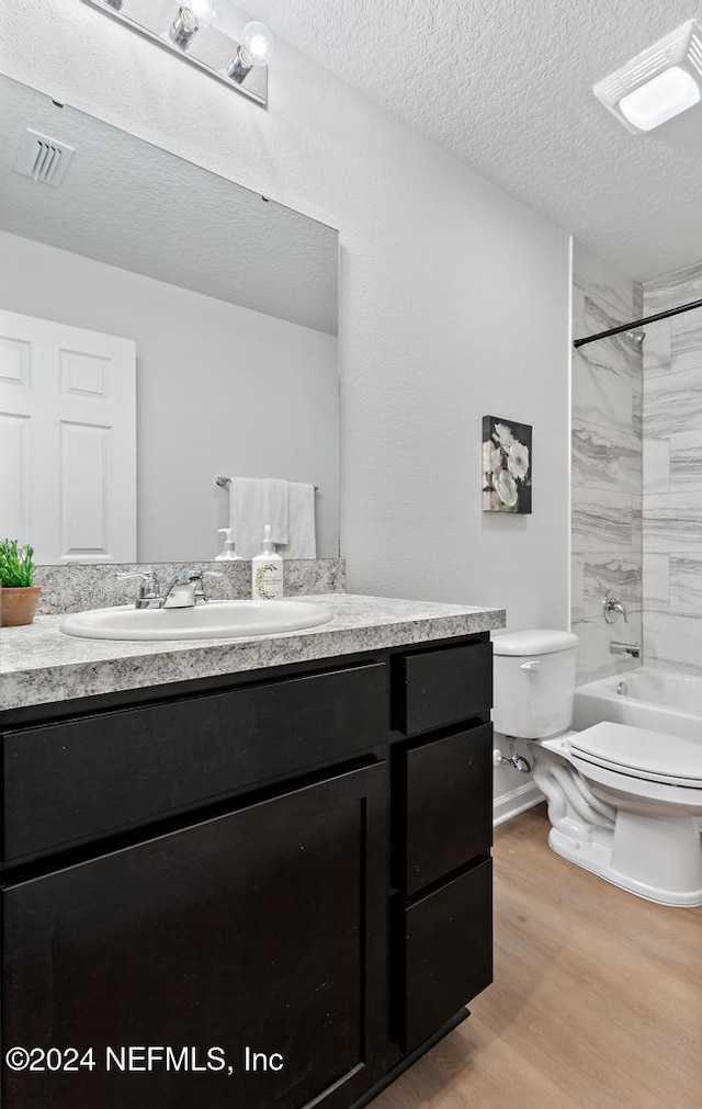 full bathroom featuring vanity, tiled shower / bath combo, toilet, a textured ceiling, and wood-type flooring