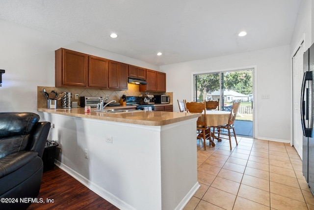 kitchen featuring kitchen peninsula, backsplash, sink, light tile patterned floors, and electric range