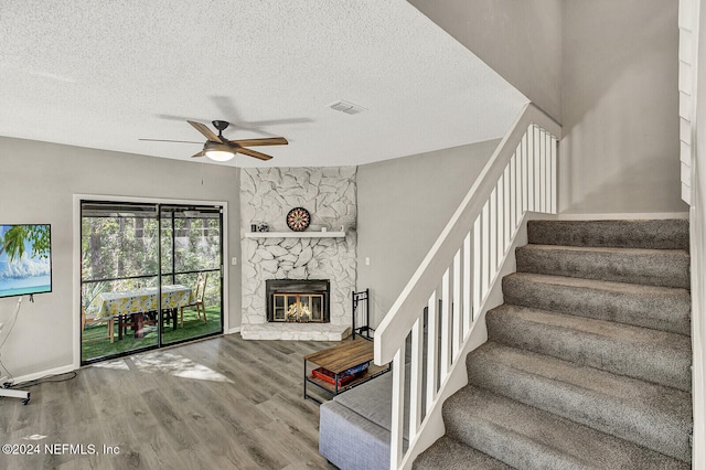 staircase featuring hardwood / wood-style floors, a textured ceiling, a stone fireplace, and ceiling fan