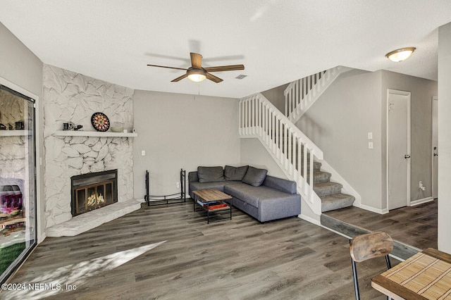 living room with a stone fireplace, ceiling fan, dark hardwood / wood-style flooring, and a textured ceiling