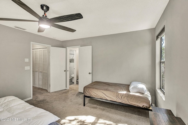 carpeted bedroom with a textured ceiling, connected bathroom, a closet, and ceiling fan