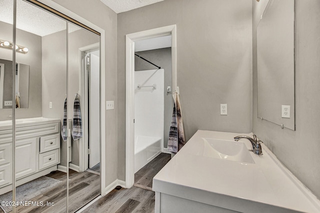 bathroom featuring hardwood / wood-style flooring, vanity,  shower combination, and a textured ceiling