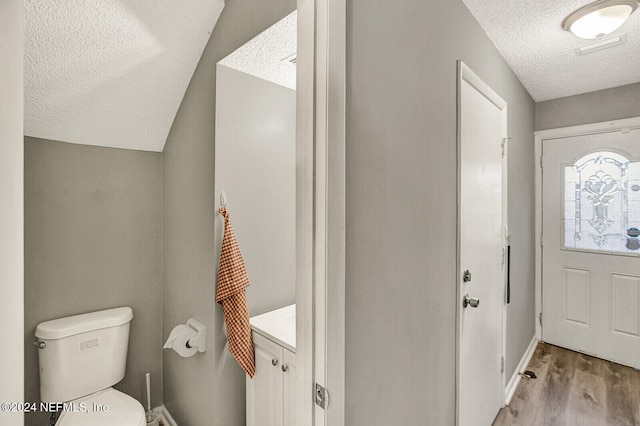 interior space featuring hardwood / wood-style floors, vanity, lofted ceiling, toilet, and a textured ceiling