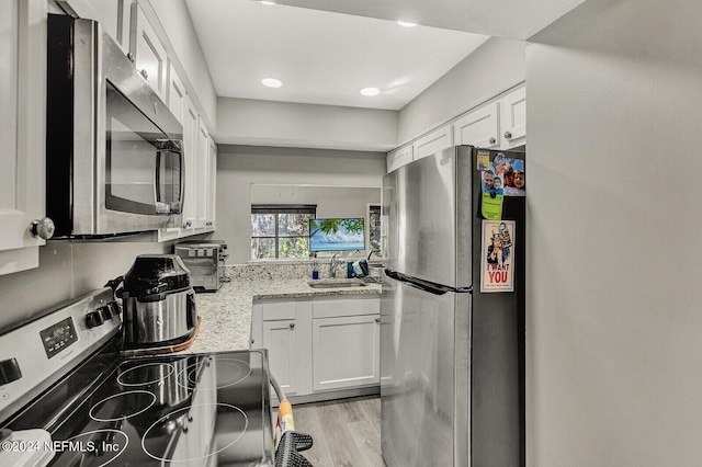 kitchen with light hardwood / wood-style floors, light stone counters, white cabinetry, and stainless steel appliances