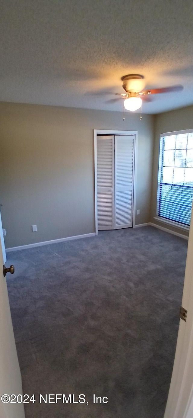 unfurnished bedroom with dark colored carpet, ceiling fan, a textured ceiling, and a closet