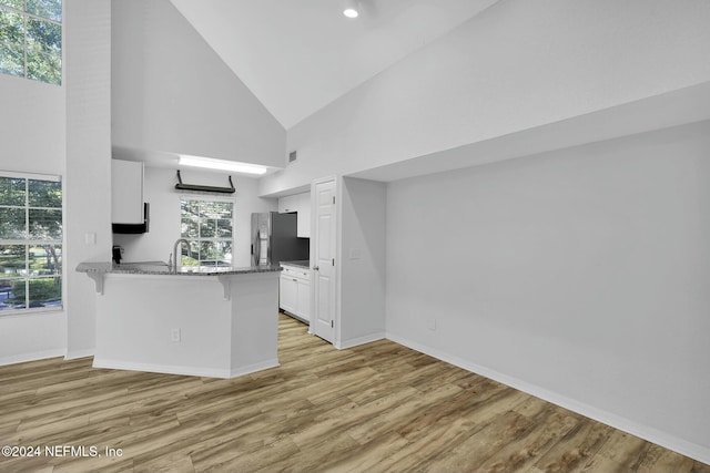 kitchen with kitchen peninsula, a breakfast bar, white cabinets, and high vaulted ceiling