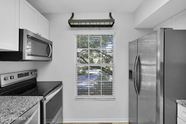 kitchen with white cabinetry, light stone counters, a textured ceiling, appliances with stainless steel finishes, and hardwood / wood-style flooring