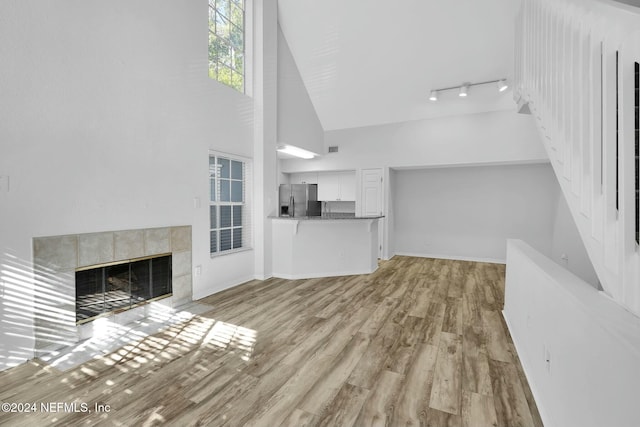 unfurnished living room featuring a fireplace, track lighting, high vaulted ceiling, and light hardwood / wood-style flooring