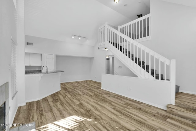 unfurnished living room featuring sink, high vaulted ceiling, track lighting, and light wood-type flooring