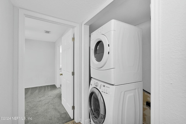 clothes washing area featuring carpet, a textured ceiling, and stacked washer and clothes dryer