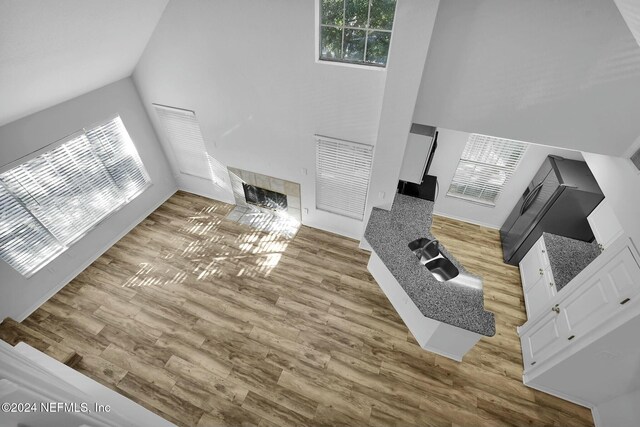 living room with sink, light hardwood / wood-style floors, high vaulted ceiling, and a tiled fireplace