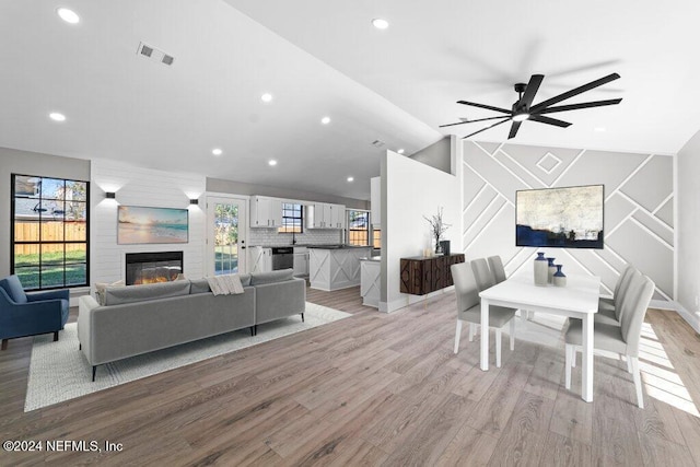 living room with ceiling fan, a large fireplace, lofted ceiling, and light wood-type flooring