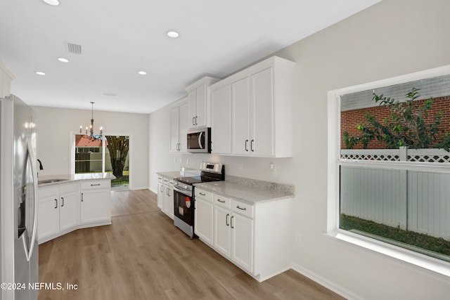 kitchen with decorative light fixtures, white cabinetry, appliances with stainless steel finishes, and light hardwood / wood-style flooring