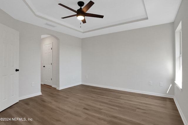 spare room featuring a tray ceiling, ceiling fan, and dark wood-type flooring