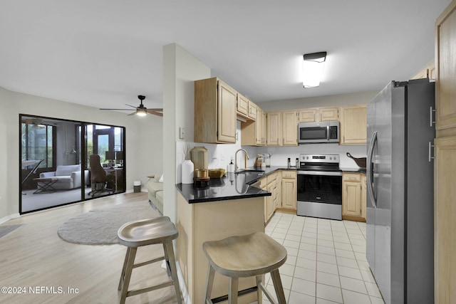 kitchen with a kitchen bar, stainless steel appliances, sink, light brown cabinets, and light tile patterned floors