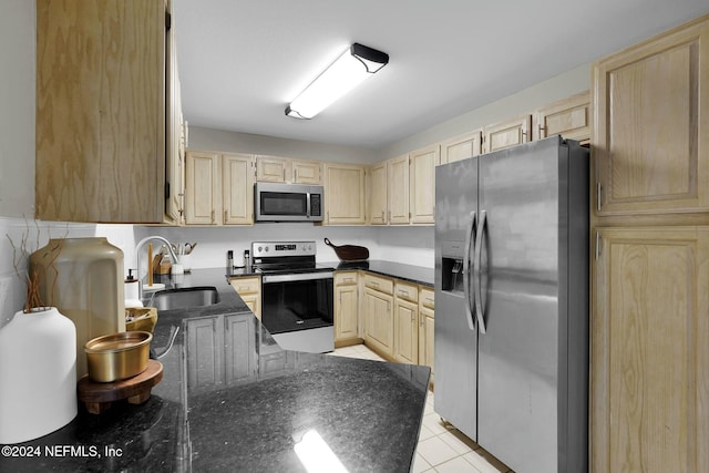 kitchen featuring light brown cabinets, sink, stainless steel appliances, dark stone counters, and light tile patterned floors