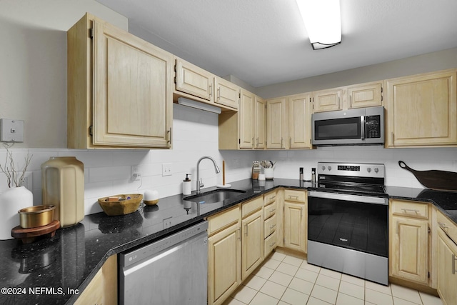 kitchen featuring light brown cabinets, stainless steel appliances, dark stone countertops, and sink