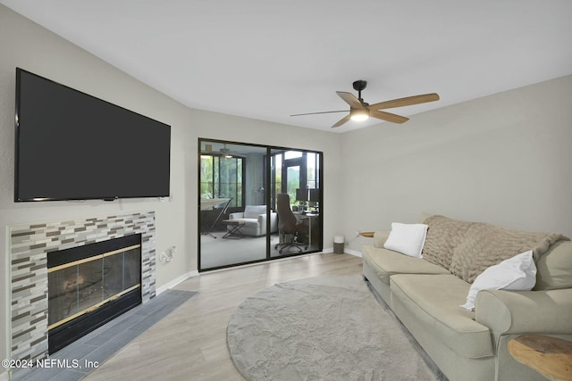 living room with light wood-type flooring, ceiling fan, and a tiled fireplace