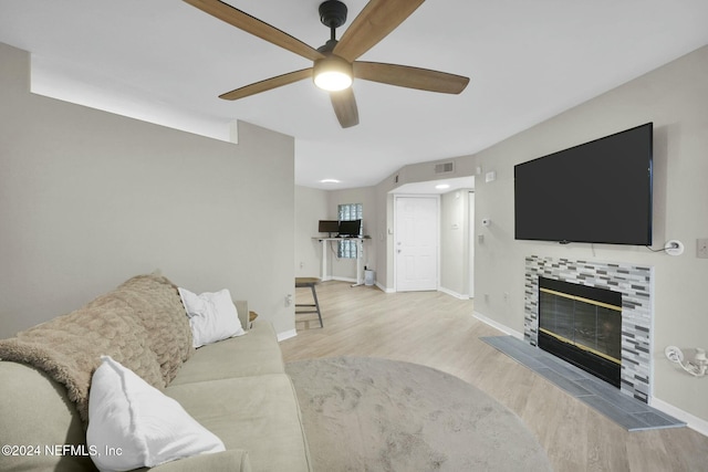 living room featuring a tiled fireplace, ceiling fan, and light wood-type flooring