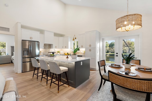 kitchen with a kitchen island, high vaulted ceiling, stainless steel refrigerator with ice dispenser, decorative light fixtures, and white cabinets