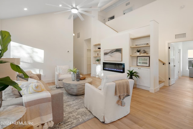 living room featuring built in shelves, light wood-type flooring, and a towering ceiling