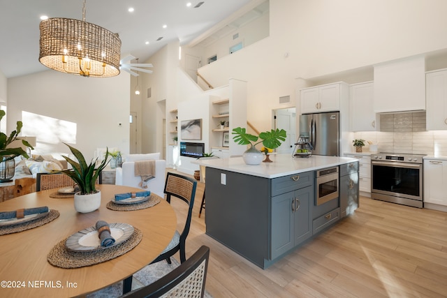 kitchen with high vaulted ceiling, white cabinets, hanging light fixtures, light hardwood / wood-style floors, and stainless steel appliances