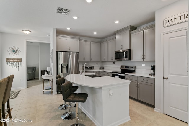 kitchen with a kitchen bar, stainless steel appliances, a kitchen island with sink, and gray cabinetry