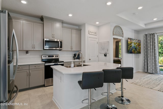 kitchen with gray cabinetry, sink, an island with sink, appliances with stainless steel finishes, and a breakfast bar area