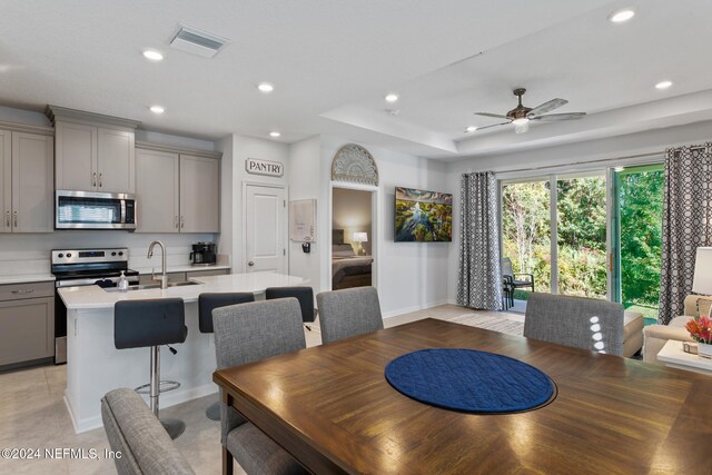 dining space with a raised ceiling, ceiling fan, and sink