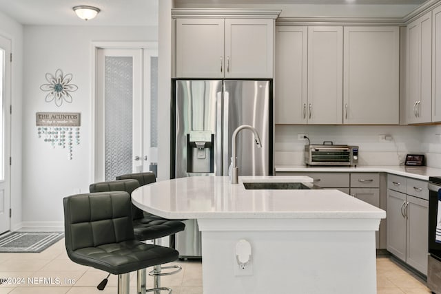 kitchen with a center island with sink, sink, gray cabinets, light tile patterned flooring, and stainless steel fridge with ice dispenser