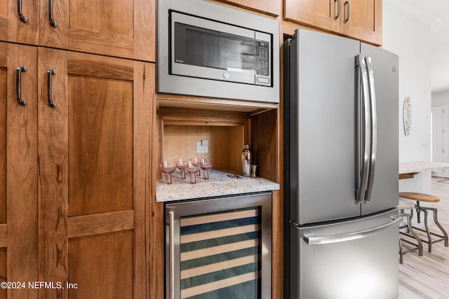 1869 S 2nd St, Jacksonville Beach, FL 32250 - kitchen featuring appliances with stainless steel finishes, wine cooler, light wood-style floors, brown cabinetry, and light stone countertops