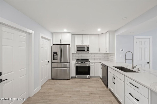 kitchen featuring sink, appliances with stainless steel finishes, white cabinetry, light stone counters, and light wood-type flooring