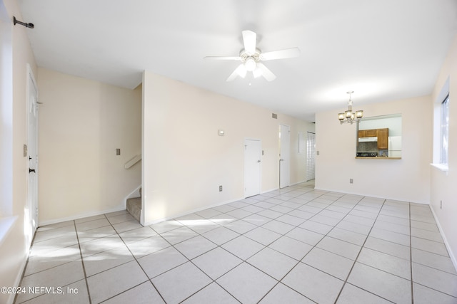 empty room with light tile patterned floors and ceiling fan with notable chandelier