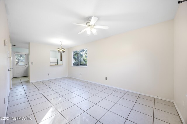 tiled empty room featuring ceiling fan with notable chandelier