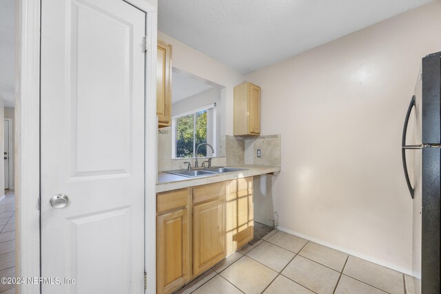 kitchen featuring light brown cabinets, refrigerator, light tile patterned floors, and sink