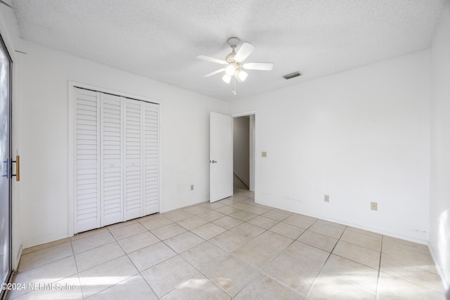 unfurnished bedroom with a textured ceiling, a closet, ceiling fan, and light tile patterned flooring