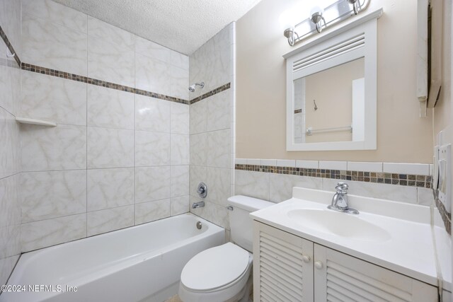 full bathroom with vanity, tiled shower / bath combo, toilet, a textured ceiling, and tile walls