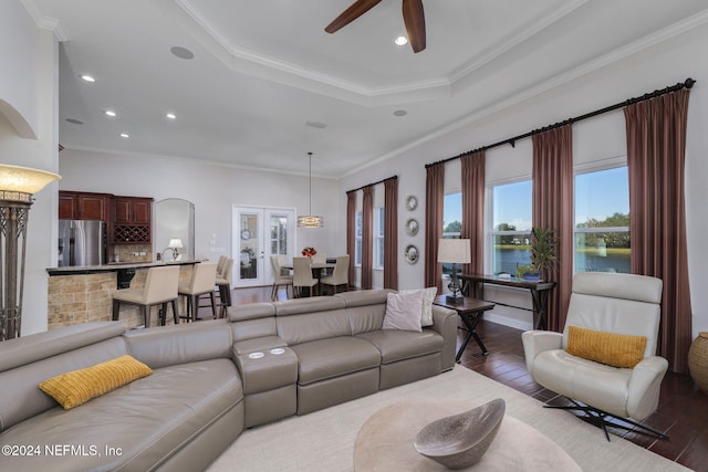 living room with a water view, a tray ceiling, wood finished floors, and ornamental molding