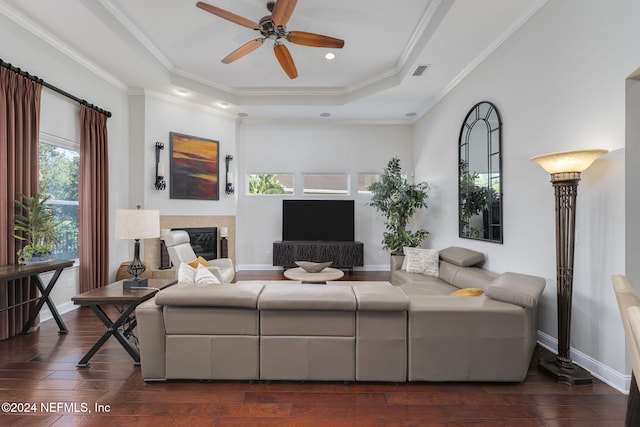 living area featuring baseboards, a raised ceiling, dark wood finished floors, a glass covered fireplace, and ornamental molding