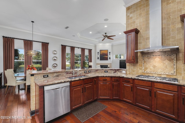 kitchen featuring a peninsula, wall chimney exhaust hood, appliances with stainless steel finishes, and a sink