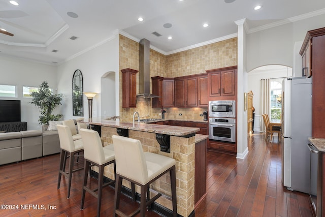 kitchen featuring arched walkways, stainless steel appliances, wall chimney range hood, and a kitchen bar