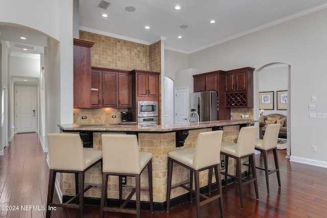 kitchen with arched walkways, stainless steel appliances, a breakfast bar, and dark wood-type flooring