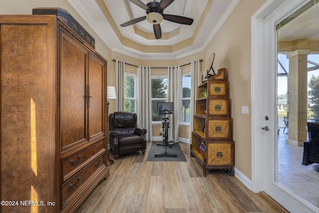 exercise area with crown molding, a raised ceiling, ceiling fan, light wood-type flooring, and baseboards