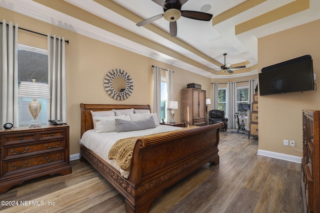 bedroom featuring baseboards, a raised ceiling, a ceiling fan, wood finished floors, and crown molding