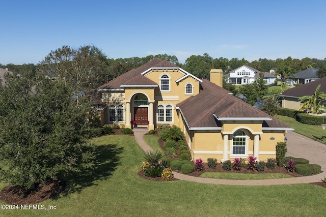 mediterranean / spanish house featuring a chimney, a front lawn, and stucco siding