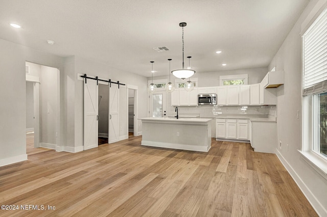 kitchen with a barn door, light hardwood / wood-style flooring, white cabinetry, hanging light fixtures, and an island with sink