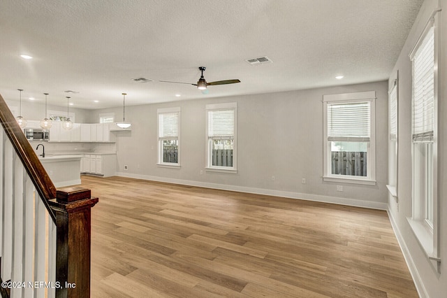 unfurnished living room featuring a textured ceiling, light hardwood / wood-style flooring, a wealth of natural light, and sink