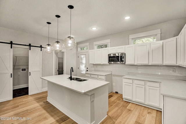 kitchen featuring a center island with sink, a barn door, white cabinetry, and sink