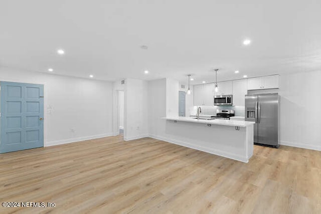 kitchen with kitchen peninsula, appliances with stainless steel finishes, decorative light fixtures, light hardwood / wood-style flooring, and white cabinetry